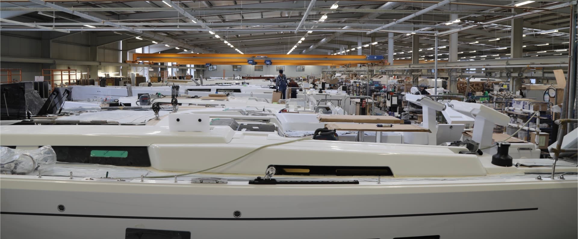 Vue grand angle de l'usine de production de Hanse Yachts avec diverses coques de yachts et des pièces en cours d'assemblage, des ouvriers engagés dans des processus de fabrication, représentant l'artisanat derrière la construction de bateaux.